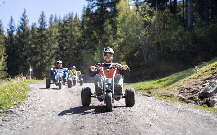 Adrenaline-filled mountain cart descent through alpine forest trail | © Dorfgasteiner Bergbahnen AG Group rides mountain carts downhill on gravel path through forested alpine terrain | © Dorfgasteiner Bergbahnen AG