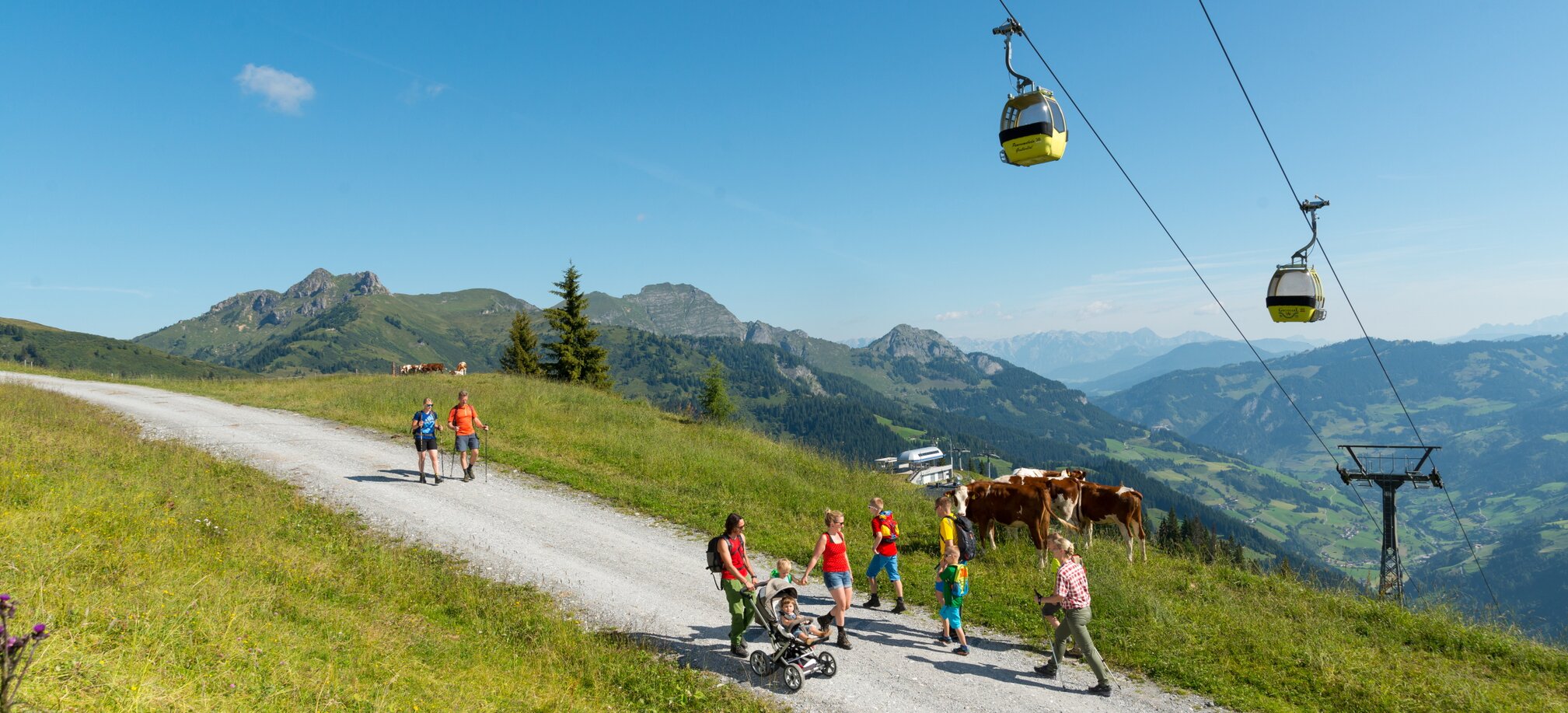 Menschen spazieren auf einer Schotterstraße unter einer Kabinenseilbahn den Berg hinauf | © Gruber Michael