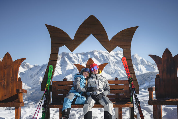Skiing in the Hochkönig ski region | © Christian Schartner Two people in ski outfits sit on a wooden bench with a crown frame & marvel at the panorama | © Christian Schartner