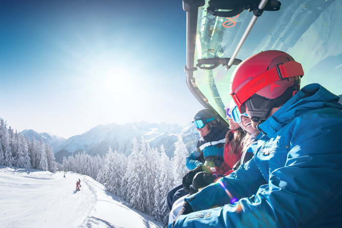 Skifahrer auf Sessellift mit Panoramablick | © Ski amadé Gruppe von Skifahrern mit Helmen und Skibrillen fährt auf einem Sessellift mit Wetterschutzhaube über eine verschneite Berglandschaft. | © Ski amadé