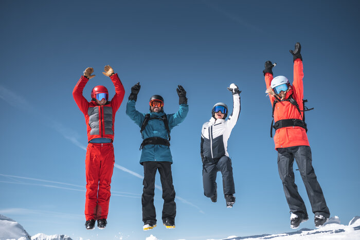 Jumping into a ski day with friends at Ski amadé | © Ski amadé Four skiers jump into the air at the same time with blue sky and snowy peaks behind them | © Ski amadé