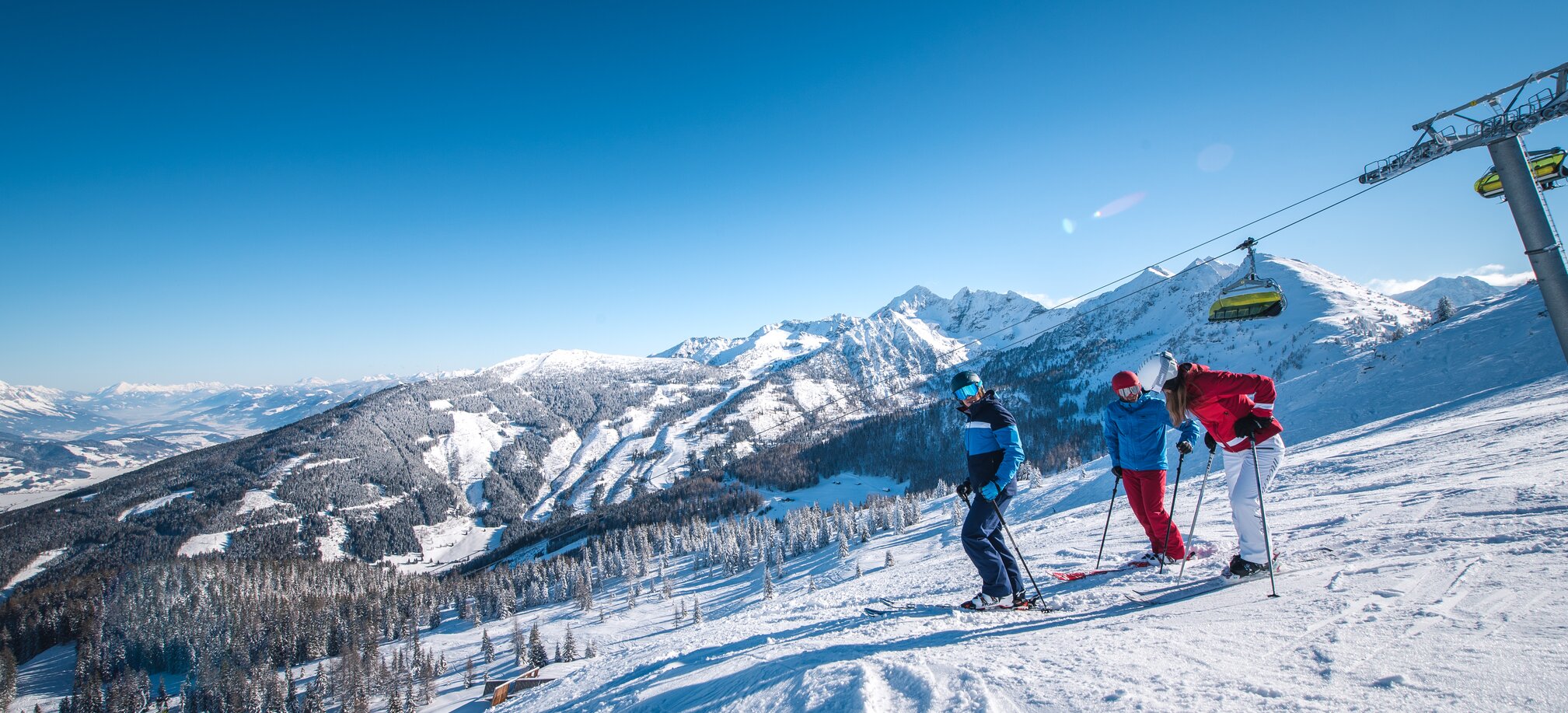 Drei Skifahrer stehen auf einer Piste mit Blick auf verschneite Berge. | © Ski amadé